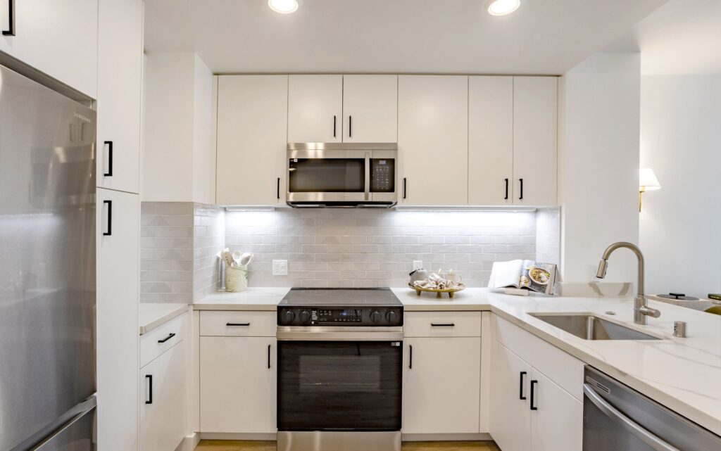 Modern kitchen with white cabinets, stainless steel appliances, electric stove, microwave, under-cabinet lighting, subway tile backsplash, and a double sink with a sleek faucet.